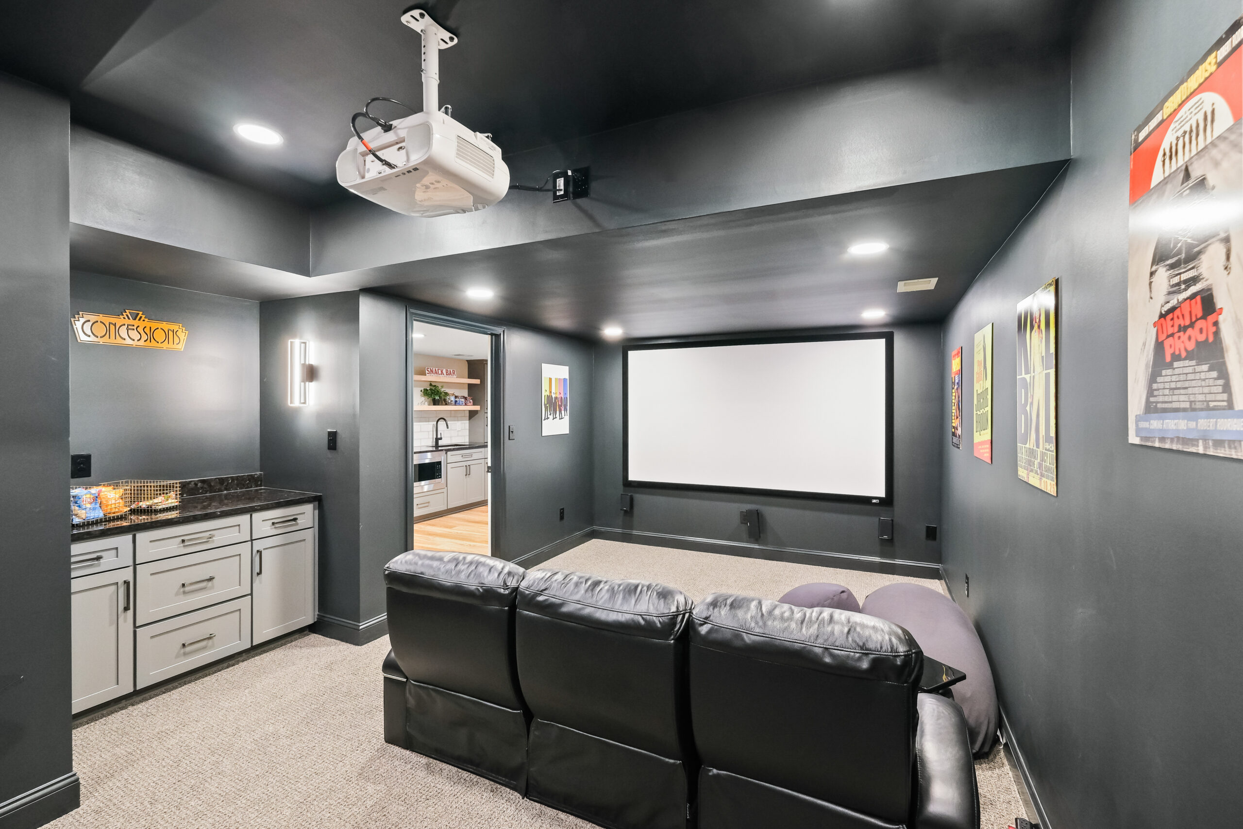 Stylish and Cozy Murrysville Home Movie Theater with Large Screen, Black Leather Couch, Cabinetry, Dark Walls and Light Carpet Creating an Intimate Setting