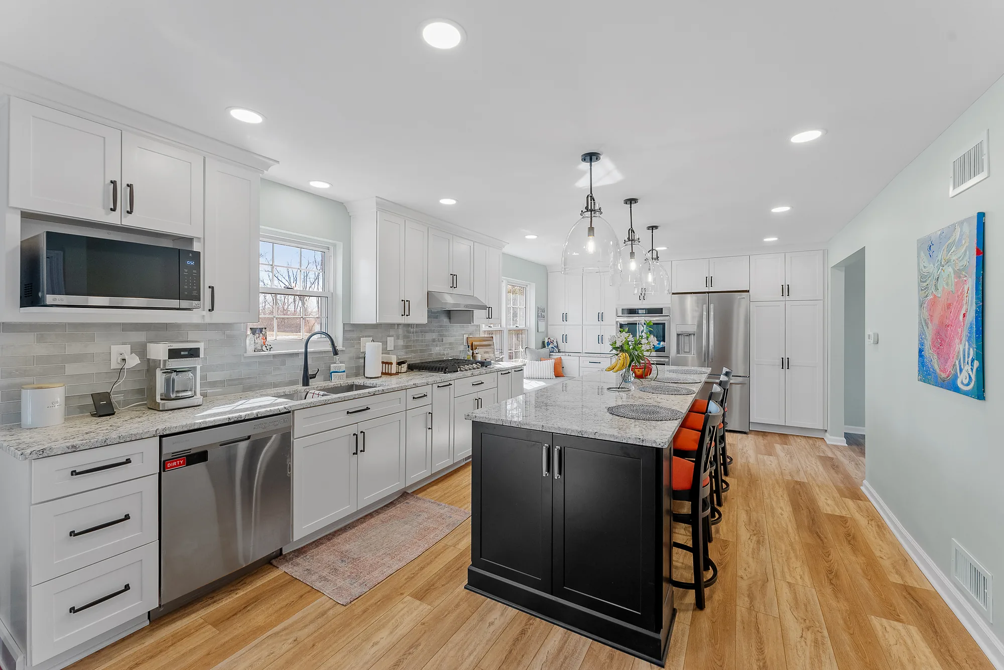 Transitional O’Hara Township Kitchen Featuring White Shaker-Style Cabinets, Warm Light and Medium Gray Countertops, Black Island and Light Wood Floor.